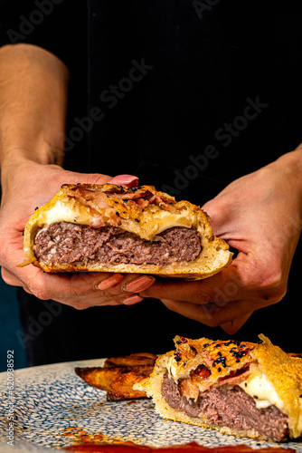 hamburguesa de ternera con mucho queso apretada por las manos de una persona 