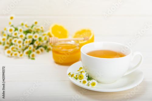 Chamomile herbal tea with flower buds  honey and lemon on a white wooden table and a bouquet of chamomile. Useful herbal  soothing drinks and natural healer concept. Immunity tea.Close up. Copy space.