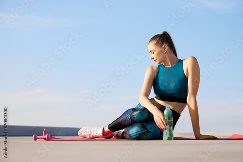 Hydration. Young beautiful woman in stylish, comfortable sport leggings and top sitting on fitness man after training outdoors on sunny day