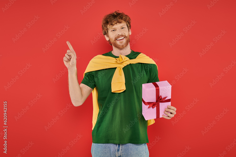 celebration, happy redhead man with beard posing in casual attire on coral background, holding gift box, festive occasions, present, fashion and trend, happiness, holiday, pointing with finger celebration, happy redhead man with beard posing in casual attire on coral background, holding gift box, festive occasions, present, fashion and trend, happiness, holiday, pointing with finger