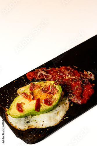 plato gourmet con aguacate, huevo y bacon sobre plato negro 