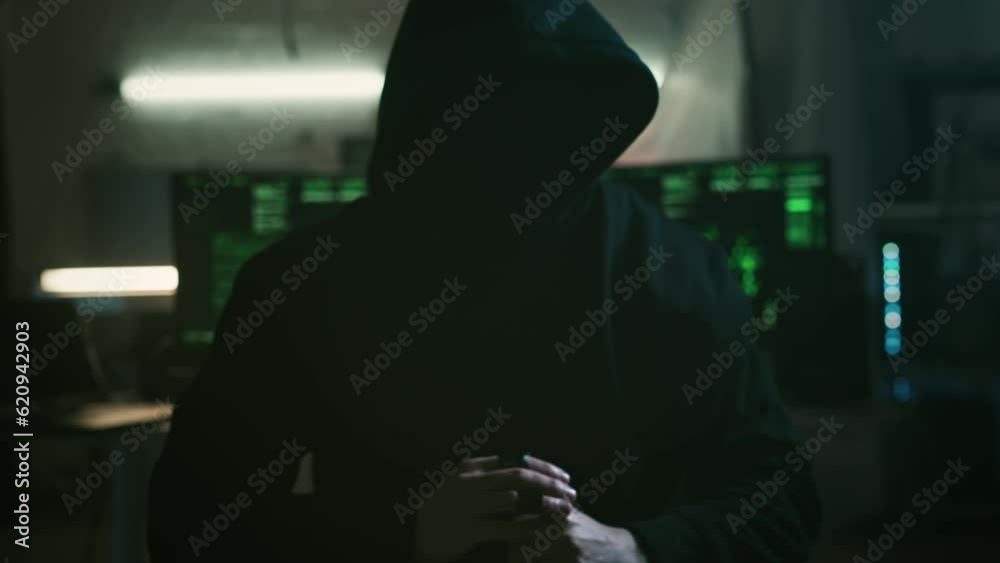 Mysterious cyber security hacker in hoodie in headquarter with computers