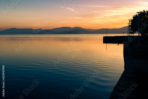 Serene lake in Portinho Da Vila (Imbituba - SC, Brazil), with a dock on the right side and mountains in the background, reflecting on the tranquil waters photo
