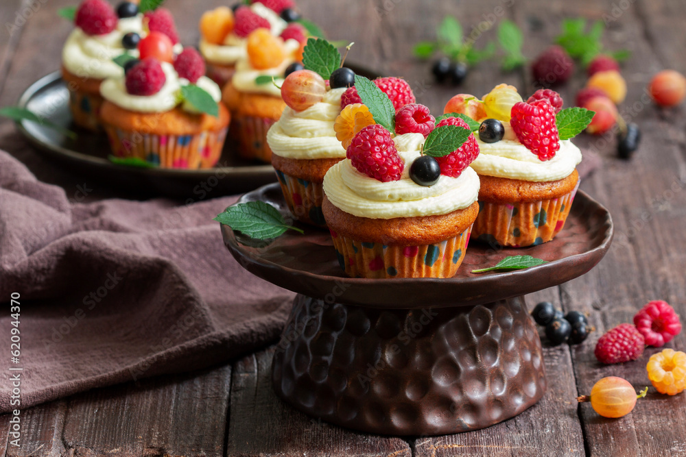 Cupcakes with butter cream and raspberry curd, decorated with berries on a wooden surface.