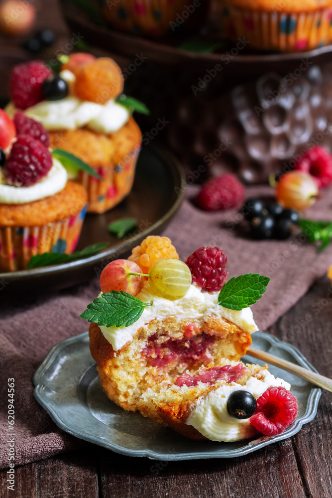 Cupcakes with butter cream and raspberry curd, decorated with berries on a wooden surface.