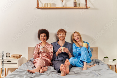 non traditional family concept, polygamy, redhead man and interracial women in pajamas holding cups of coffee, morning routine, bisexual, understanding, three adults, cultural diversity, acceptance