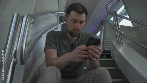 Male commutes in dual deck train seated on flyer and surfing internet. Man travels on doubledecker railroad train while sitting on staircase because there are no empty seats in summer in Europe.  photo