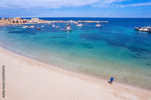 Aerial view of tourist standing in an empty white sand beach looking at the sea in front of the fishing village of Marzamemi, Marzamemi, Pachino municipality, Siracusa province, Sicily photo