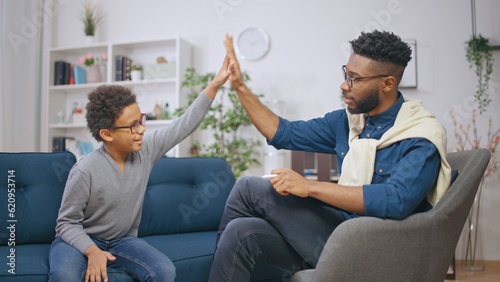 African American psychologist and a happy boy giving each other high five after successful session