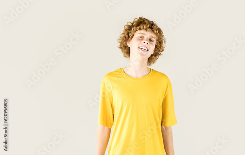 Smiling curly guy in yellow T-shirt on neutral background with copy space. Studio photography. photo