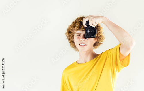 Curly hair young man photographer looks through the camera viewfinder on neutral gray background with copy space. Advertising of photography courses mockup template. Studio photography.