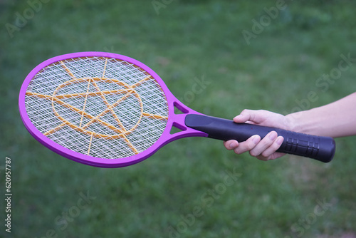 Closeup hand holds mosquito electric swatter racket. Concept, electric device to kill mosquitoes, insects, bugs by swatting to flying insects.          photo