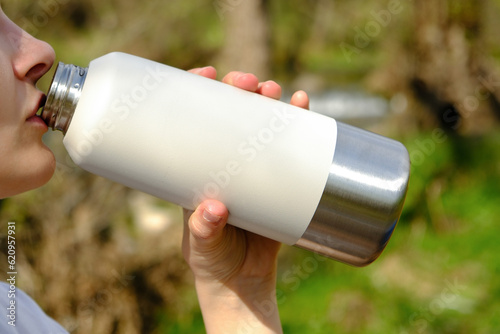 Portrait of a woman drinking water from a bottle outdoor in woods, hydrate concept