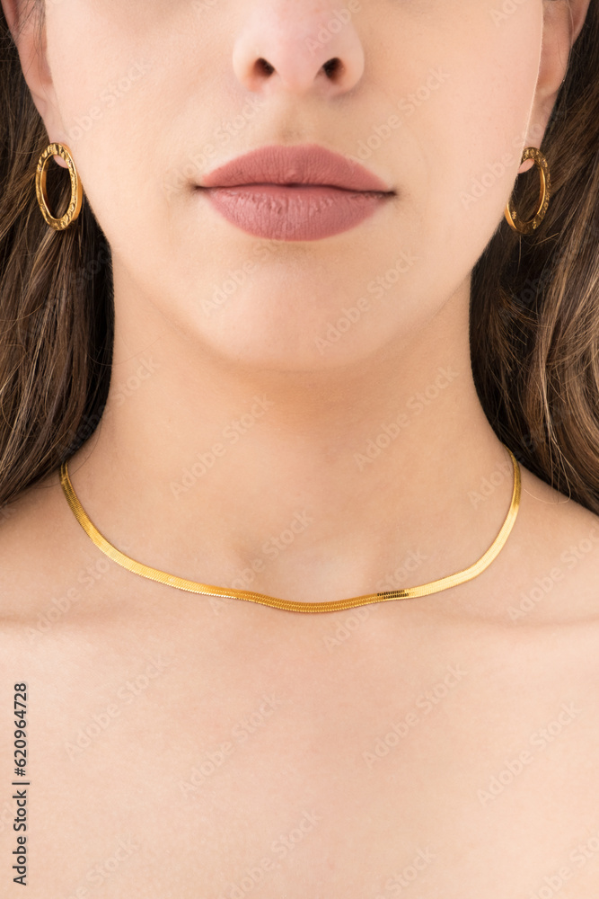 Young woman wearing golden earrings and snake chain necklace.