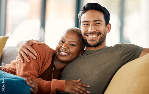Happy hug, interracial couple and portrait on a sofa at home with love and care in a living room. Woman, young people and together in a house sitting on a lounge couch relax with support and embrace
