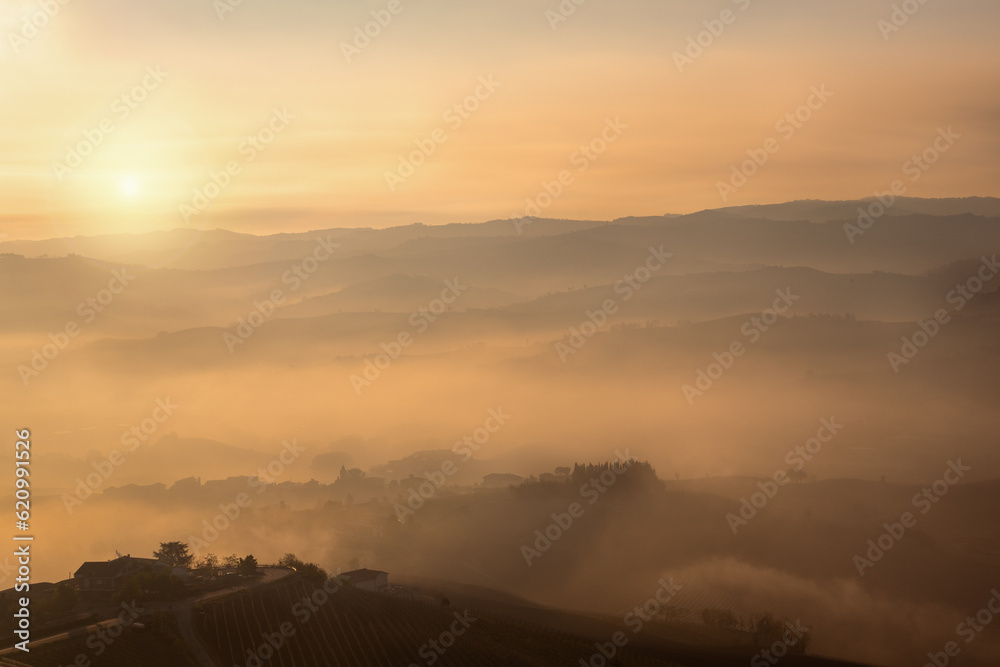 Scenic sunset and sunrise over the Langhe hills, peace and tranquillity. Sky with clouds and fog coloured orange, wonderful