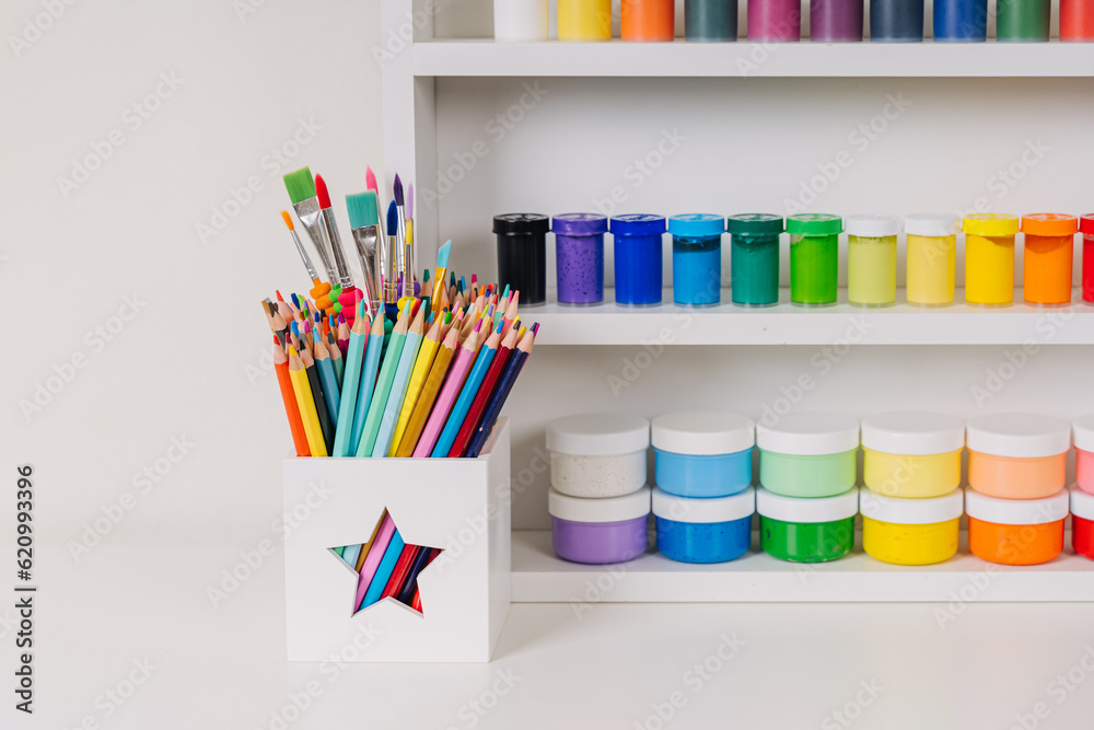Obraz premium Paints and pencils on white shelves. Stationery and supplies for drawing and craft. Various material for creativity and kids art activity. Organizing and storage in craft room.