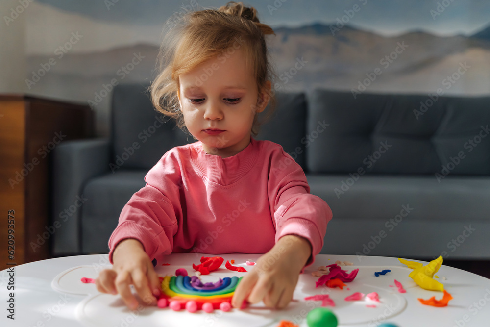 A little girl playing with rainbow from play dough for modeling. Art Activity for Kids. Fine