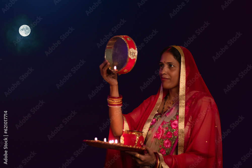 Fototapeta premium Woman looking at moon through a sieve during Karva Chauth