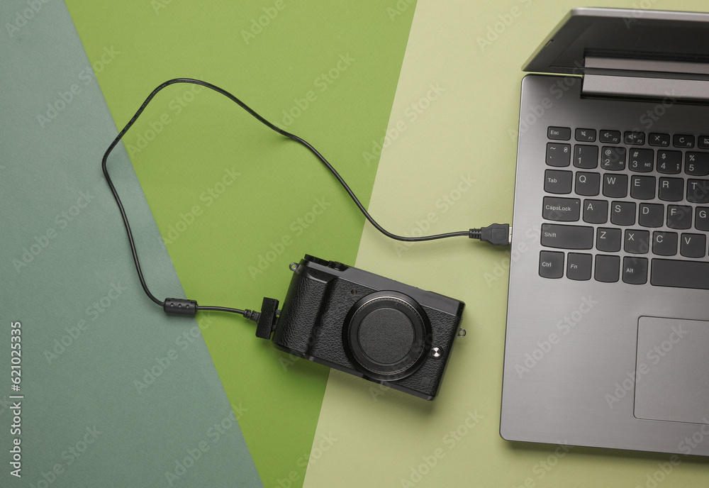 Modern camera connected by cable to laptop. Top view Modern camera connected by cable to laptop. Top view