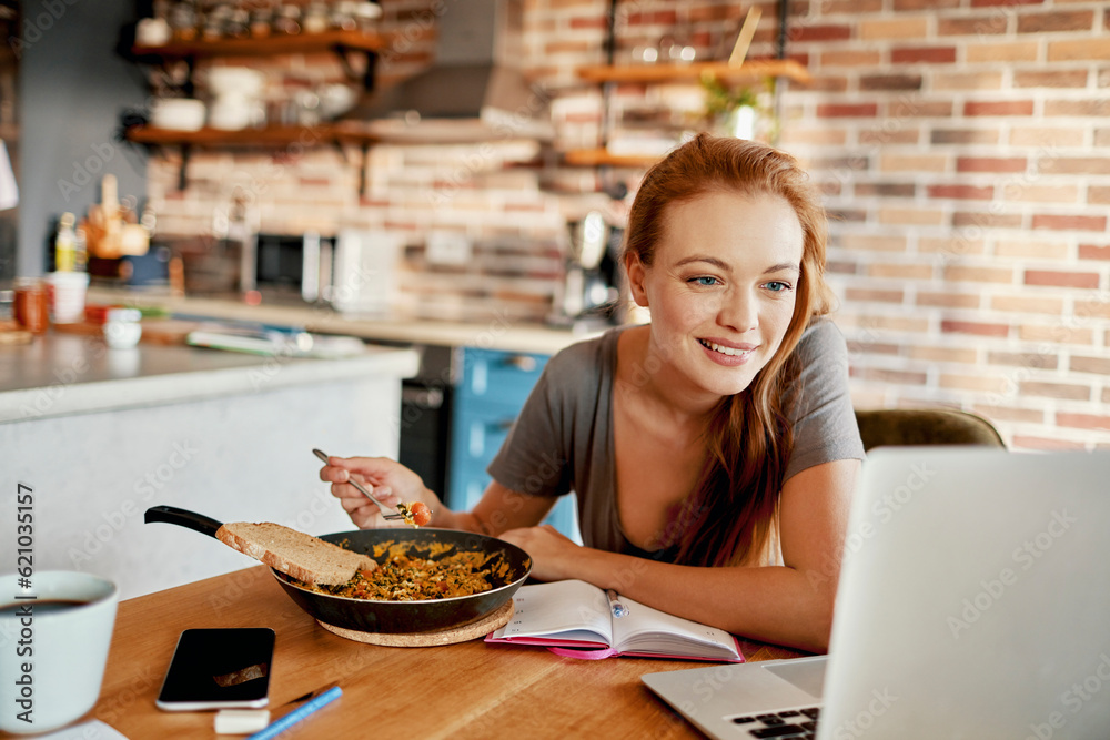 Young woman using a laptop while having breakfast in the morning