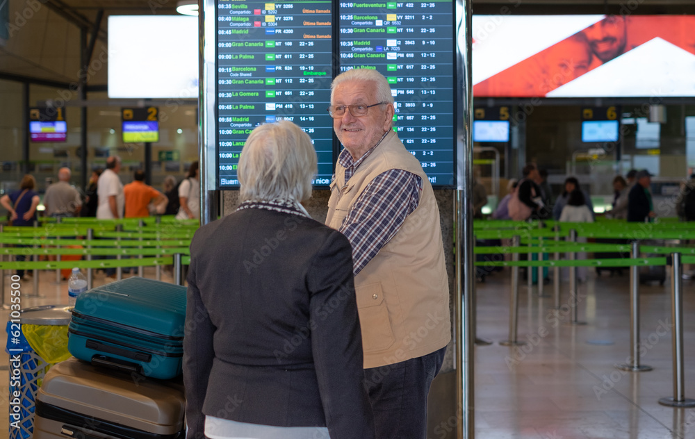 Obraz premium Back view of white haired senior couple pushing luggage trolley walking in the airport area for departure. Old senior man and woman leaving for vacation