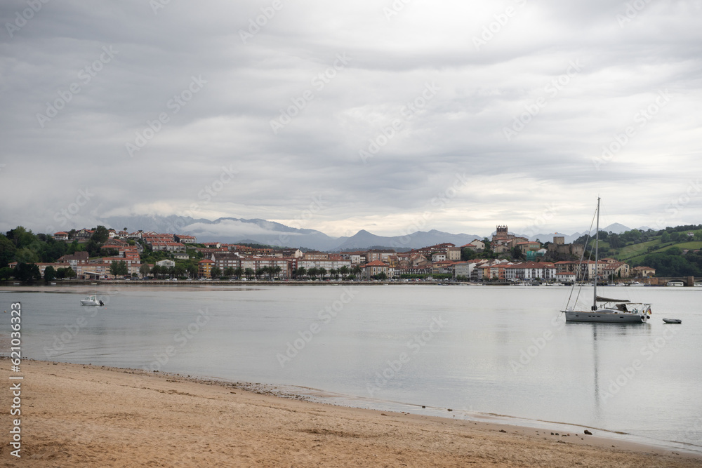 View of walled city from a beach wih boats and mountains on the background