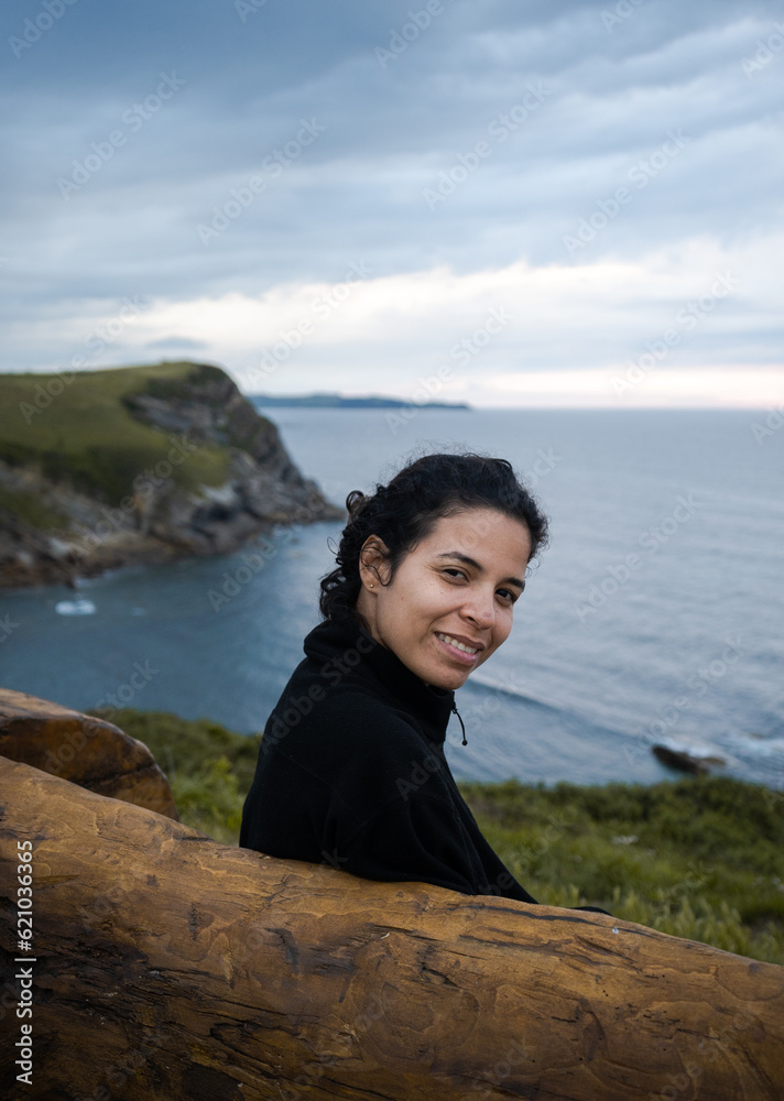Young hispanic woman smiles sitting on a bench over the beach in cold weather Young hispanic woman smiles sitting on a bench over the beach in cold weather