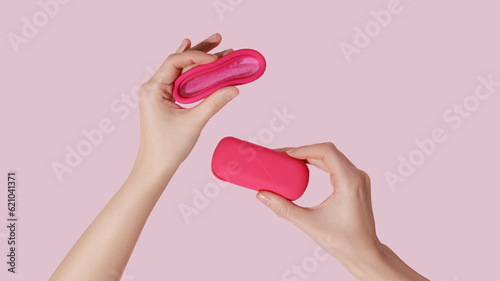 Female hand hold reusable menstrual cup and case on pink background