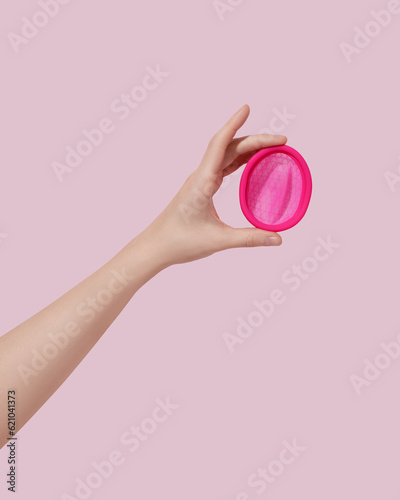 Female hand with reusable menstrual disc on pink background