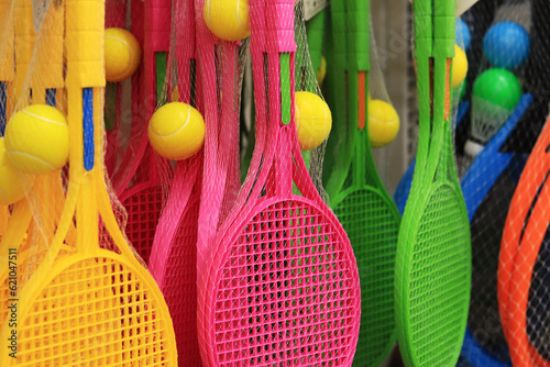 Tennis rackets in different colors in the store. Plastic tennis racket and ball in a set for sale. Bright tennis sets