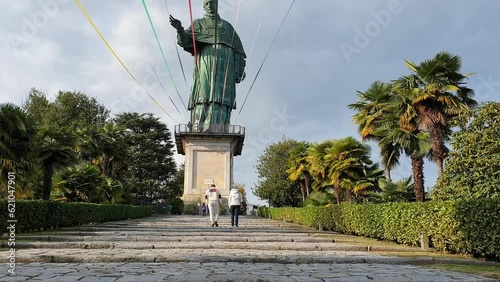 Couple walk on stairs towards giant statue of San Carlo in Arona, Italy. Slow motion photo
