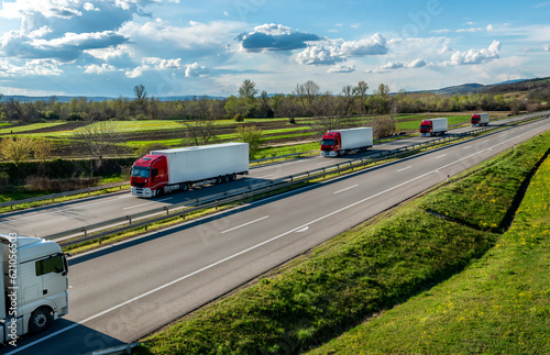 Highway transportation scene with Convoy of red and white transportation trucks in line on a rural highway under a beautiful blue sky