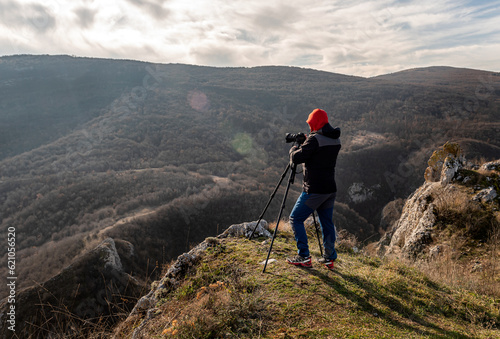 Photographer taking photographs with digital camera on a tripod in mountains. Travel and active lifestyle concept
