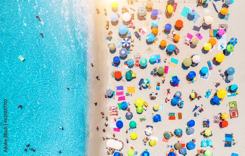 Aerial view of colorful umbrellas on sandy beach, swimming people in blue sea at sunset in summer. Sardinia, Italy. Tropical landscape with clear azure water. Travel and vacation. Top down drone view - obrazy, fototapety, plakaty 