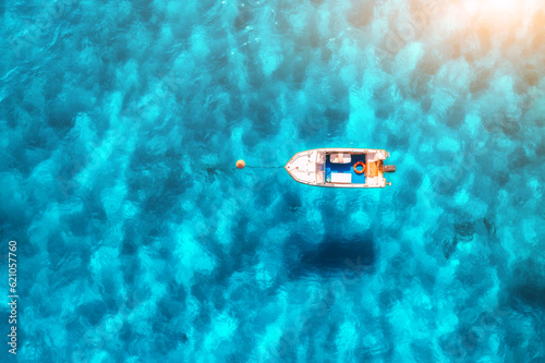 Aerial view of beautiful little boat in blue sea at sunset in summer. Sardinia, Italy. Top drone view of motorboat, ocean with transparent azure water. Travel. Tropical landscape. Yachting. Seascape
