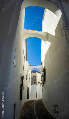 Vertical pictura of a narrow white alley of the old quarter of Arcos de la Frontera, Cadiz, Andalusia, Spain, with arches between the houses and blue sky photo