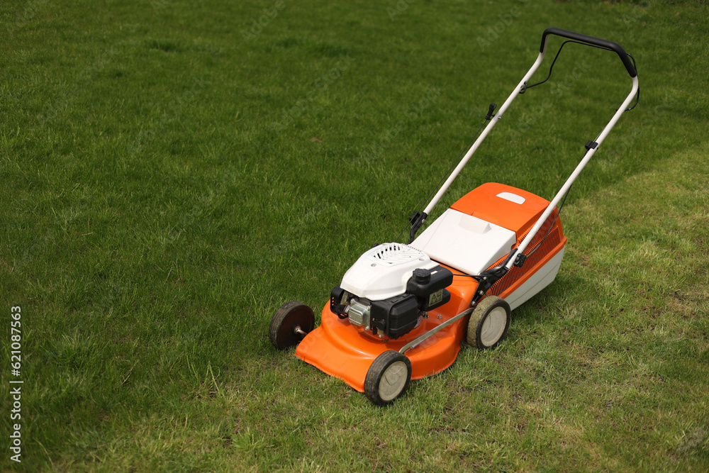 Fototapeta premium Top view of modern orange-grey electric lawn mower cutting bright lush green grass. Gardening work tools. Rotary lawn mower machine on lawn. Professional lawn care service. Place for text