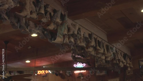 This panning video shows a collection of old hanging cow boy boots on a western bar's ceiling. photo
