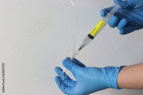 Profissional wearing gloves holding a ketamine syringe drug with liquid and injecting the drug in the intravenous acess.