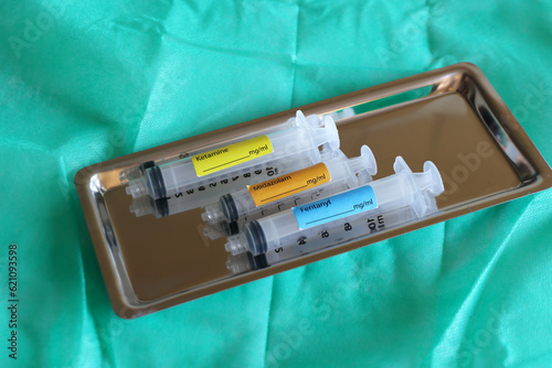 Stainless steel tray with syringe of ketamine, fentanyl and Midazolam in a green background. photo