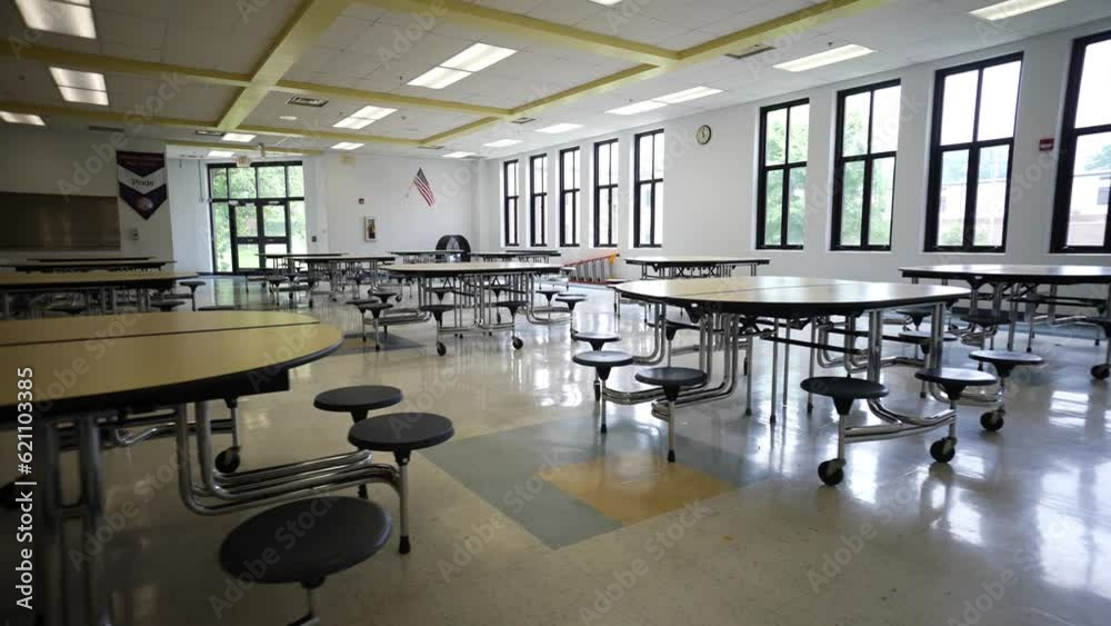 Trucking view to right showing dark and empty school cafeteria with tables and seats.