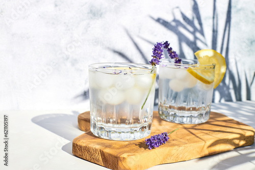 Chilled lavender lemonade with lemon and ice on a wooden stand on a gray table. Diet non-alcoholic summer cocktail. Detox water with citrus