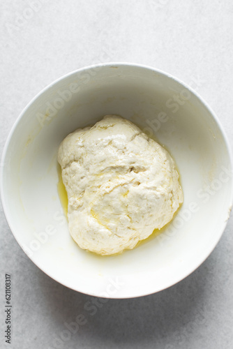 bread dough coated in olive oil, bread dough left to rise in white mixing bowl, process of making bread