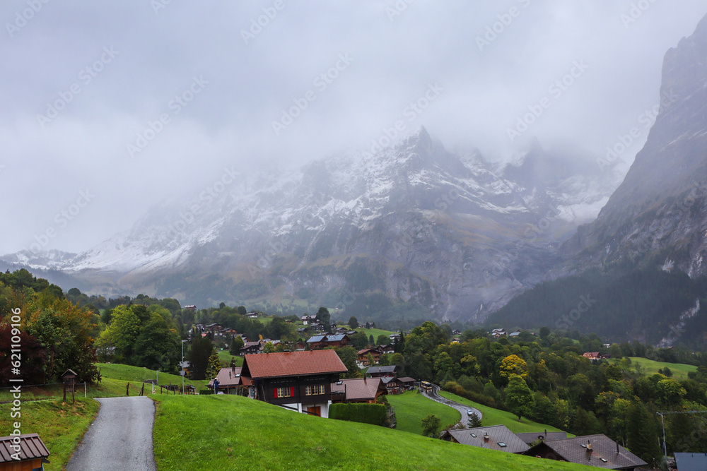 Grindelwald, Switzerland. Swiss Alps mountains landscape with fog. Photo with wooden chalet cottage on fresh green fields. 