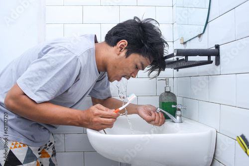 Fotografija Young man using water to clean his teeth and mouth after tooth brushing