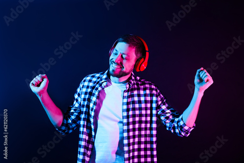 Happy man in headphones enjoying music in neon lights against dark blue background © New Africa