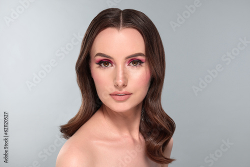 Portrait of beautiful young woman with makeup and gorgeous hair styling on light grey background