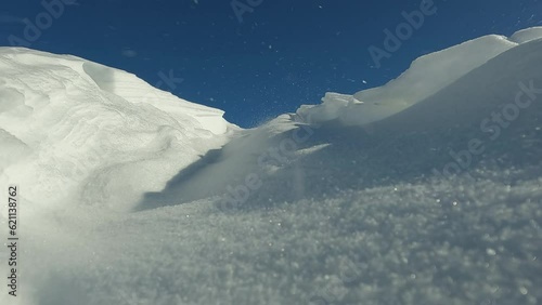 Strong winter winds blow large snow drift off mountaintop at an altitude. Snow sweeps dangerous sediments in mountains which leads to avalanches. Dangerous overhangs of snow create avalanche spots photo