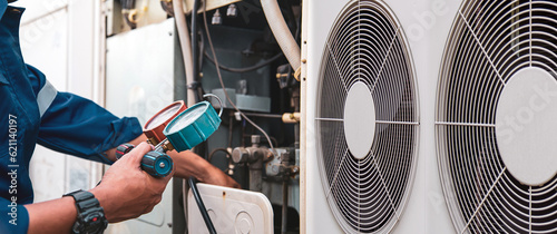 Heat and Air Conditioning, HVAC system service technician using measuring manifold gauge checking refrigerant and filling industrial air conditioner after duct cleaning maintenance outdoor compressor.